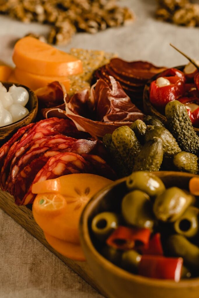 A rustic charcuterie platter featuring sliced cured meats, olives, pickles, and kumquats.