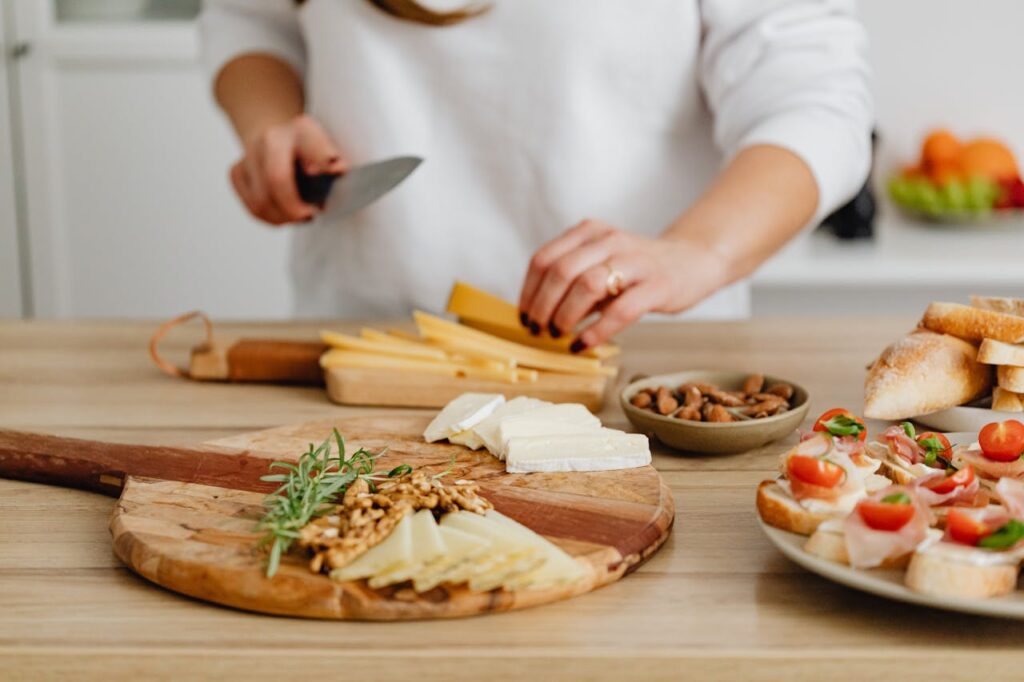 Person slicing cheese for a charcuterie board with nuts, herbs, and fresh bread.